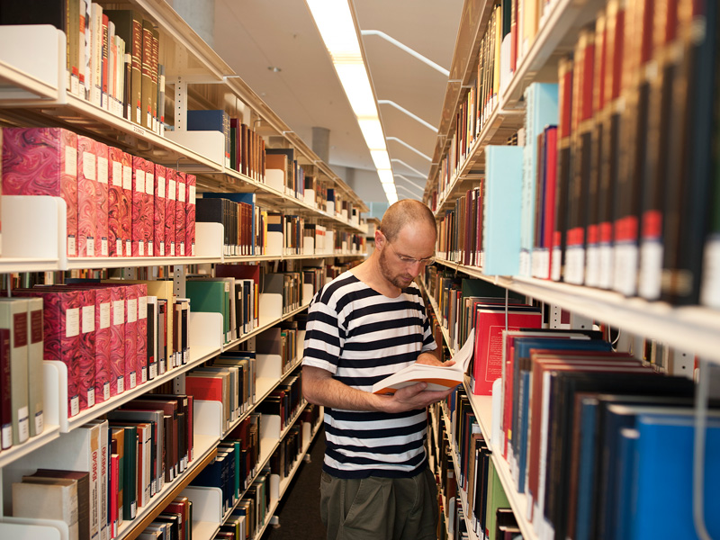 Ein Student liest ein Buch zwischen den Regalen der Universitätsbibliothek der Universität Erfurt