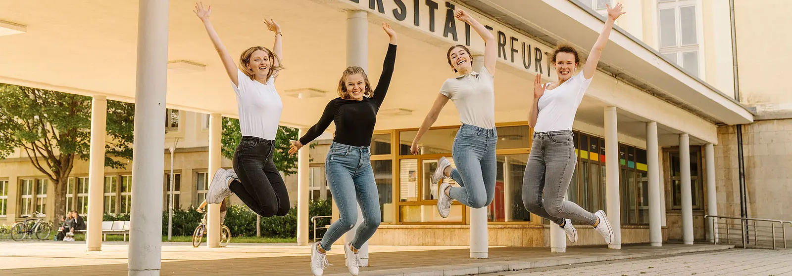 Springende Studentinnen vorm Eingangsbereich der Uni Erfurt