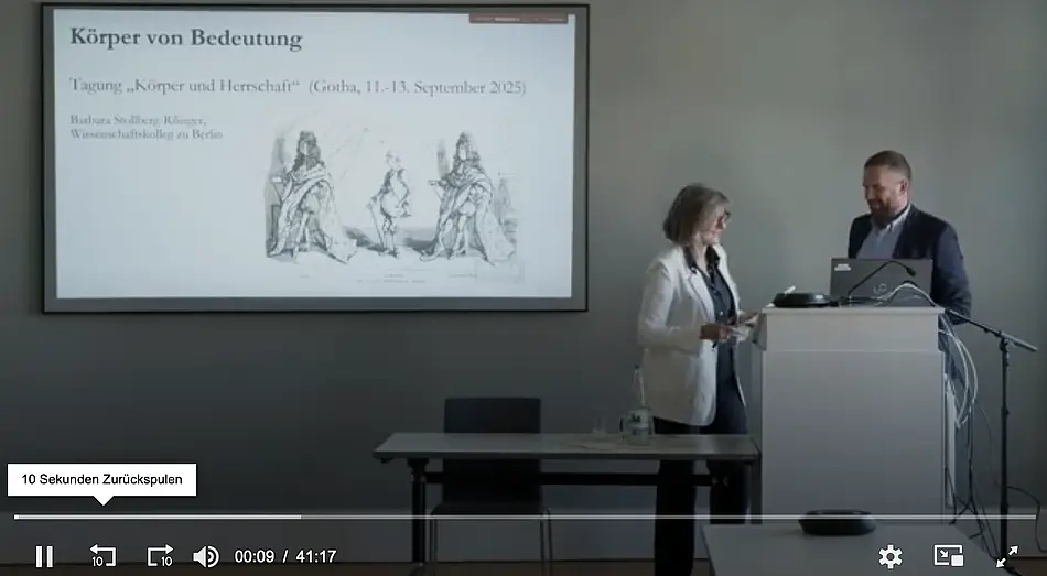 Rechts im Bild Frau am Pult, links Projektionsfläche mit Tagung- und Vortragstitel