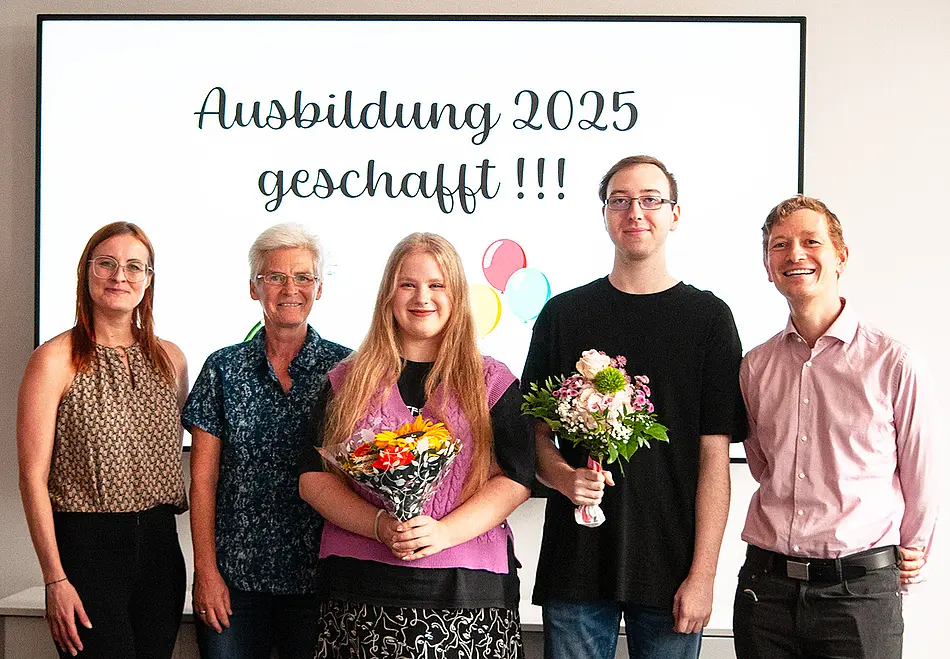 Fünf Leute lächelnd vor Monitor mit Luftballons und Schrift: Ausbildung 2025 geschafft! Auf dem Foto von links nach rechts: Christin Hoffmann, Frau Dr. Tischer, Zoe Gohlke, Florian Pegel und Herr Schümann