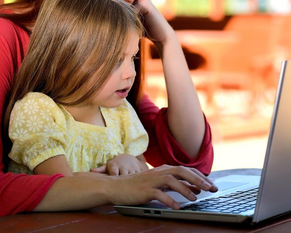 Eine junge Frau sitzt gemeinsam mit einem Kind am Laptop