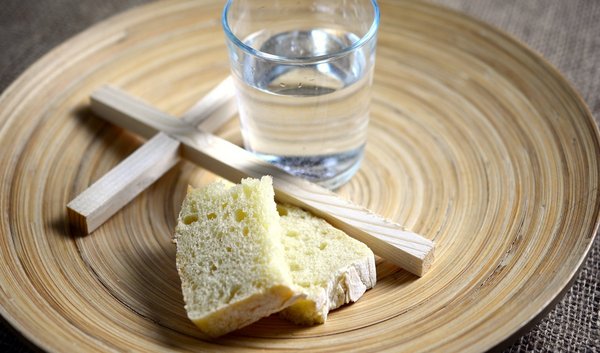 Brot und Wasser neben einem christlichen Kreuz.