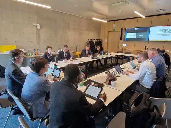 Die Teilnehmer*innen des Fachgesprächs sitzen im Konferenzraum und folgen einem per Videokonferenz gehaltenen Vortrag.