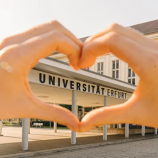 hands building a heart in front of the campus entrance