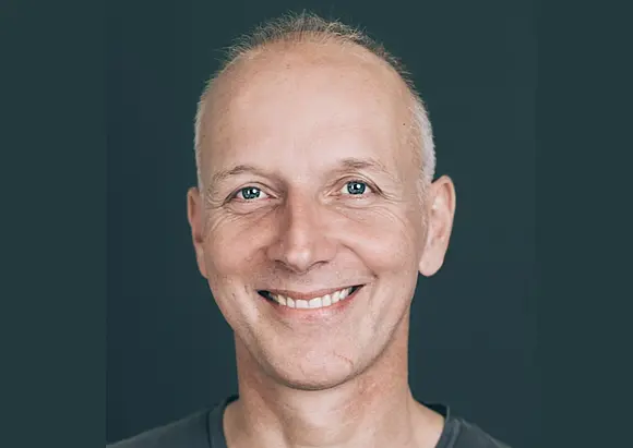 Porträtbild von Stephan Beuting, weißer Mann mit kurzen grauen Haaren, lächelnd, dunkelgrauer Hintergrund