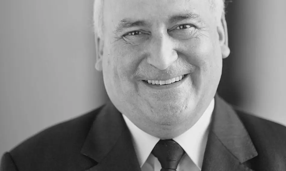 Schwarz-weiß Porträtfoto von Michael Gabel, großes Lächeln, angeschnittener Kopf, Krawatte über weißem Hemd und Jacket 