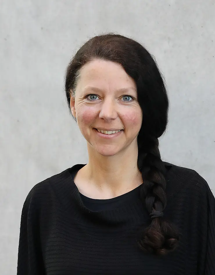 Porträtbild Katharina Leonhardt, dunkle lange Haare über die rechte Schulter gelegt, schwarzes Top, lächelt in Kamera