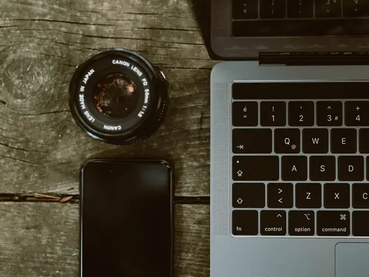 [Translate to English:] Smartphone und Kameraobjektiv neben Laptop