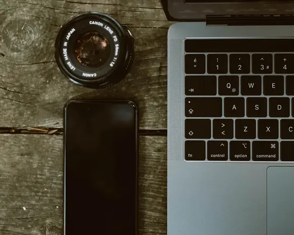 Ein Handy und ein Kameraobjektiv liegen neben einem Laptop