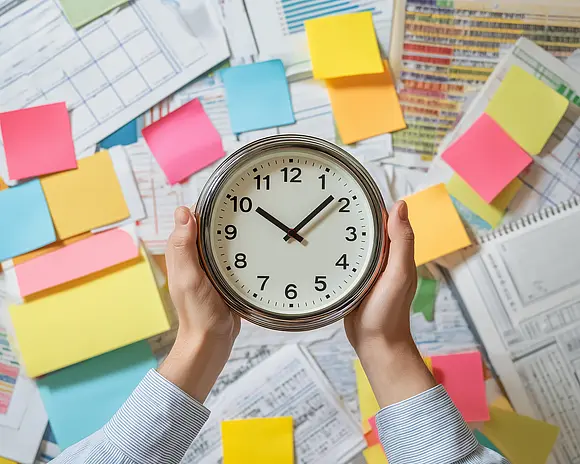Zwei Hände halten eine Wanduhr vor bunten Stickynotes