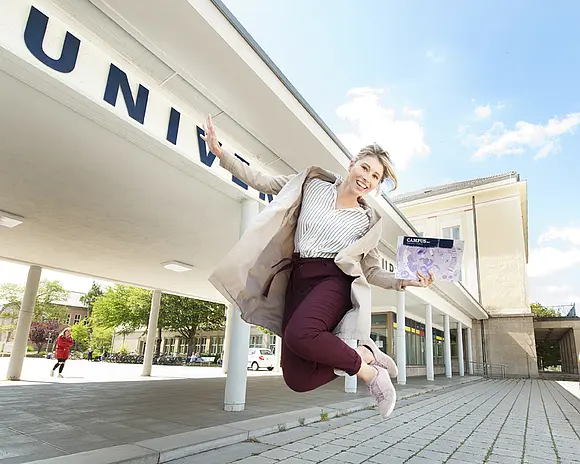 Eine Studierende hüpft vorm Haupteingang der Uni