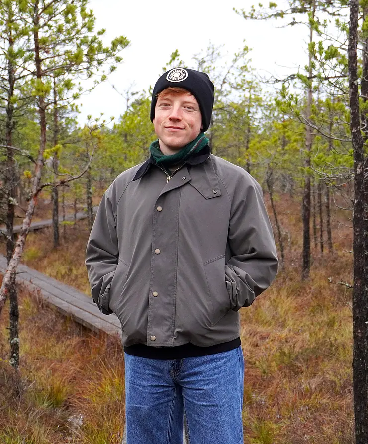 Tobias mit Jeans und grüngrauer Jacke und schwarzer Mütze bei einem Spaziergang im Wald