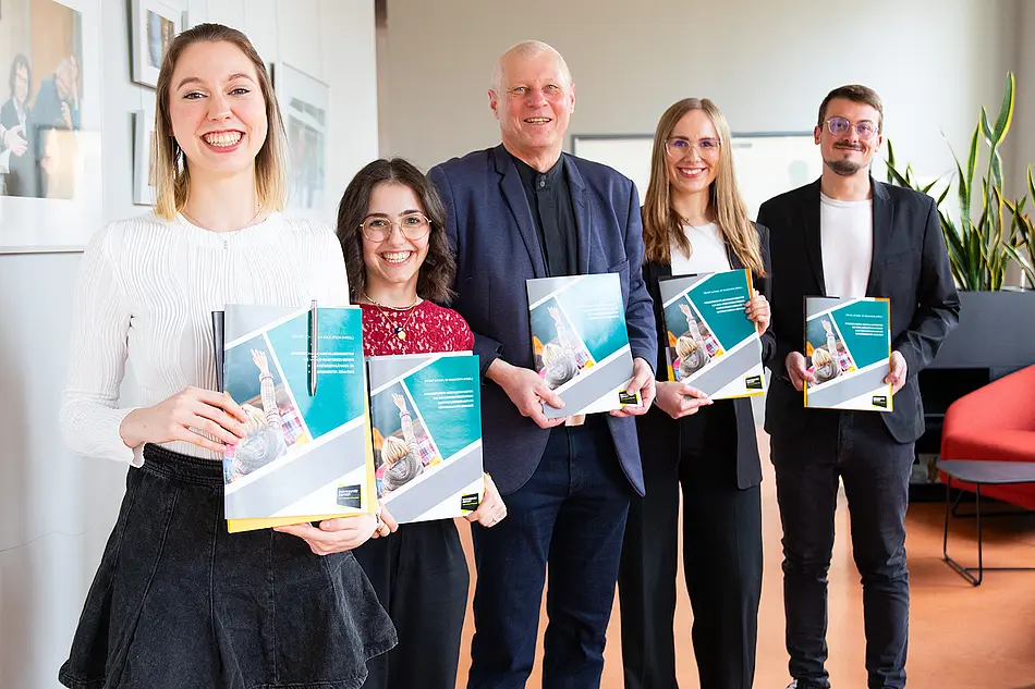 Vier strahlende ESE-Absolvent*innen mit einer ESE-Broschüre, in der Mitte Andreas Lindner
