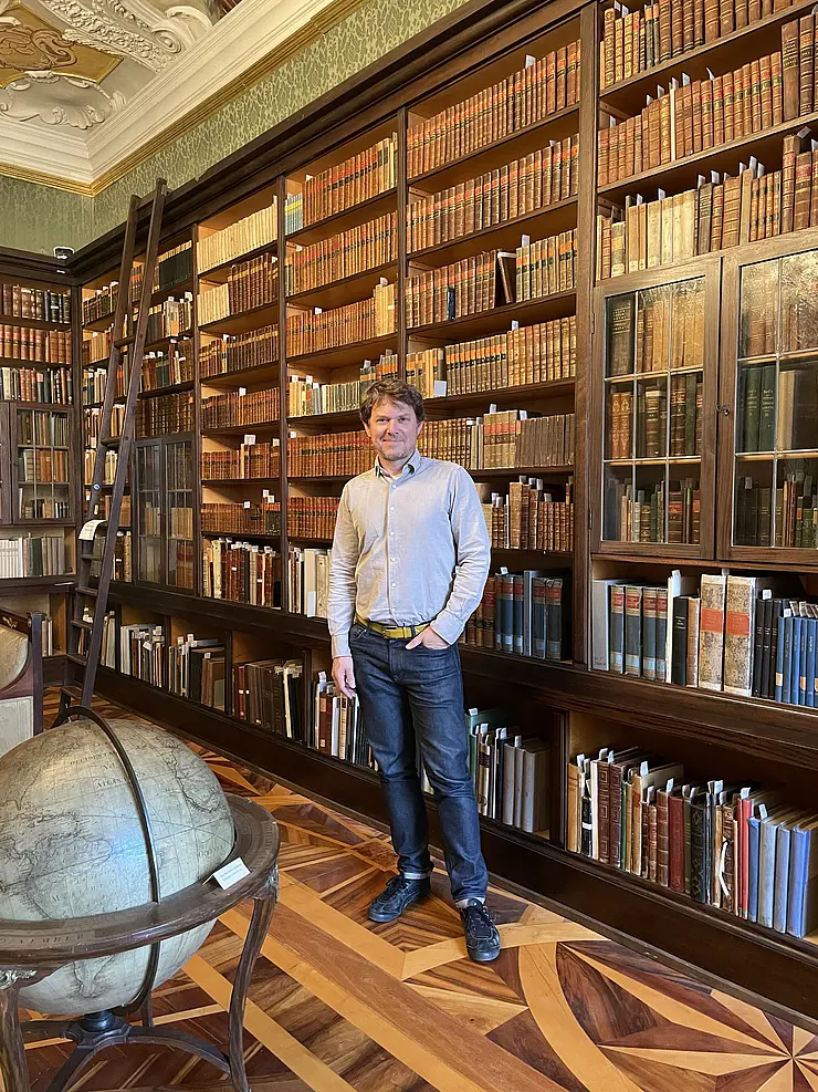 Man stands in front of ceiling-high shelves in library room