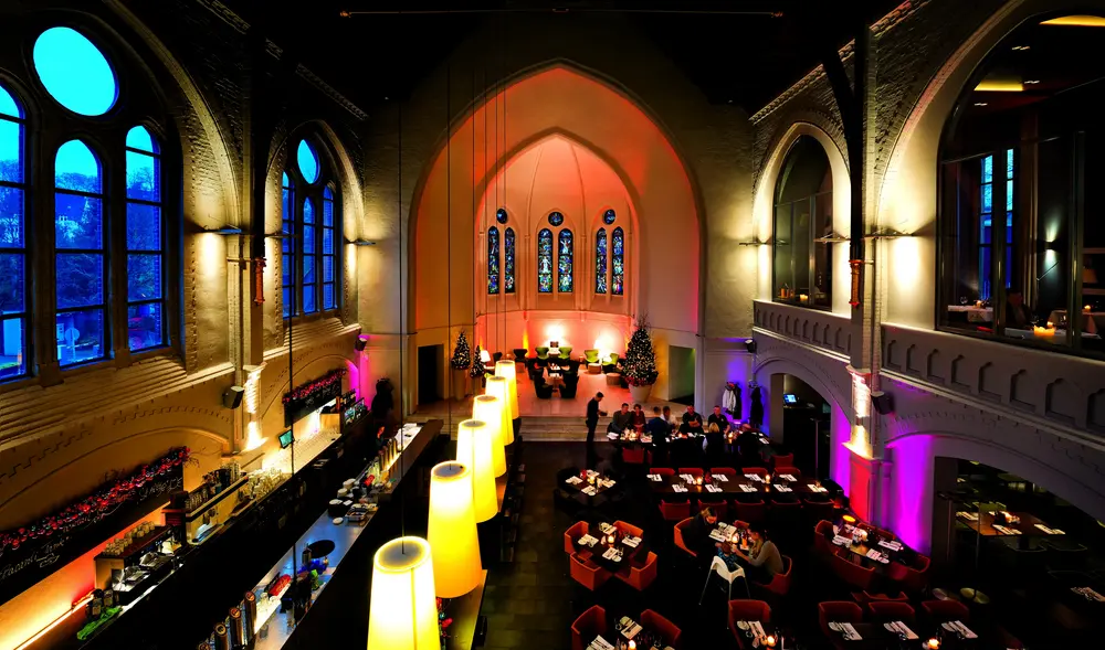 Innenansicht des Restaurants "Glück und Seligkeit" in Bielefeld, das einen Kirchenraum in ein modernes Restaurant mit gedämmten Licht und dunkler Holzeinrichtung umgewandelt hat