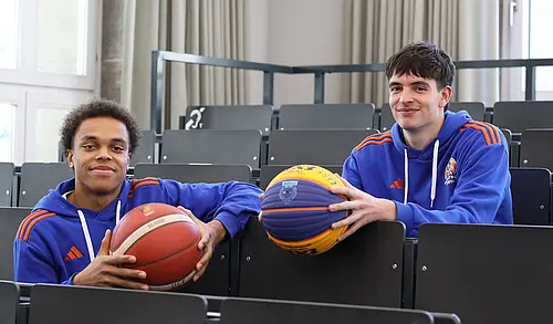 Zwei Basketballer mit je einem Ball sitzen im Hörsaal