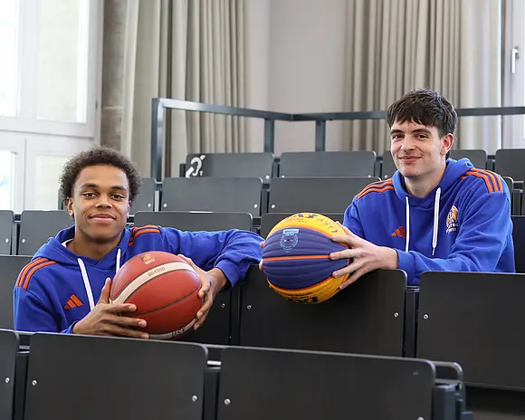 Zwei Basketballer mit je einem Ball sitzen im Hörsaal