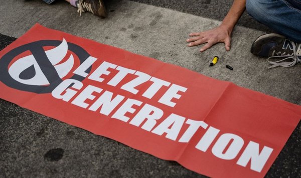 Ein Transparent der Letzten Generation neben Demonstranten, die sich mit den Händen auf die Straße geklebt haben