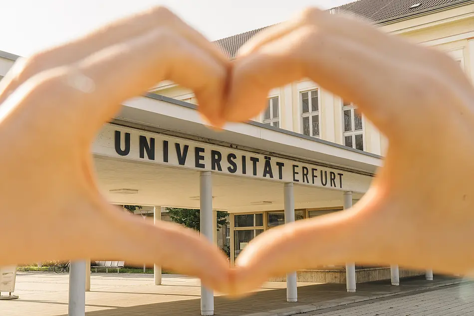 Zwei Hände bilden ein Herz vor dem Eingang zur Universität Erfurt.