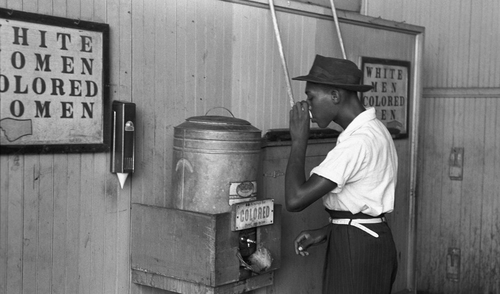 Ein Afroamerikaner trinkt von einem Wasserspender für Farbige