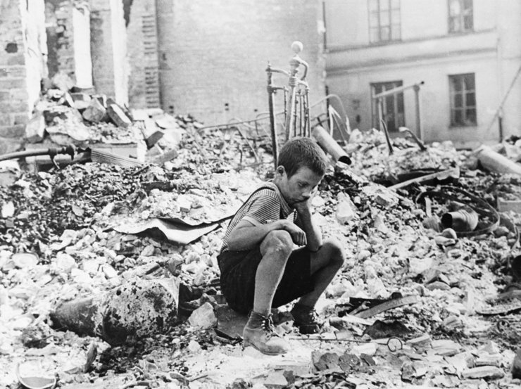 Kind sitzt vor Trümmerhaufen