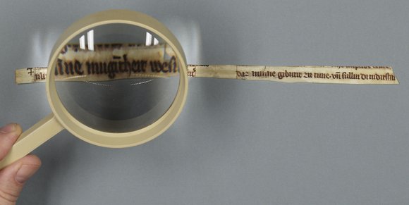 Fragment einer Meister Eckhart Handschrift durch eine Lupe betrachtet