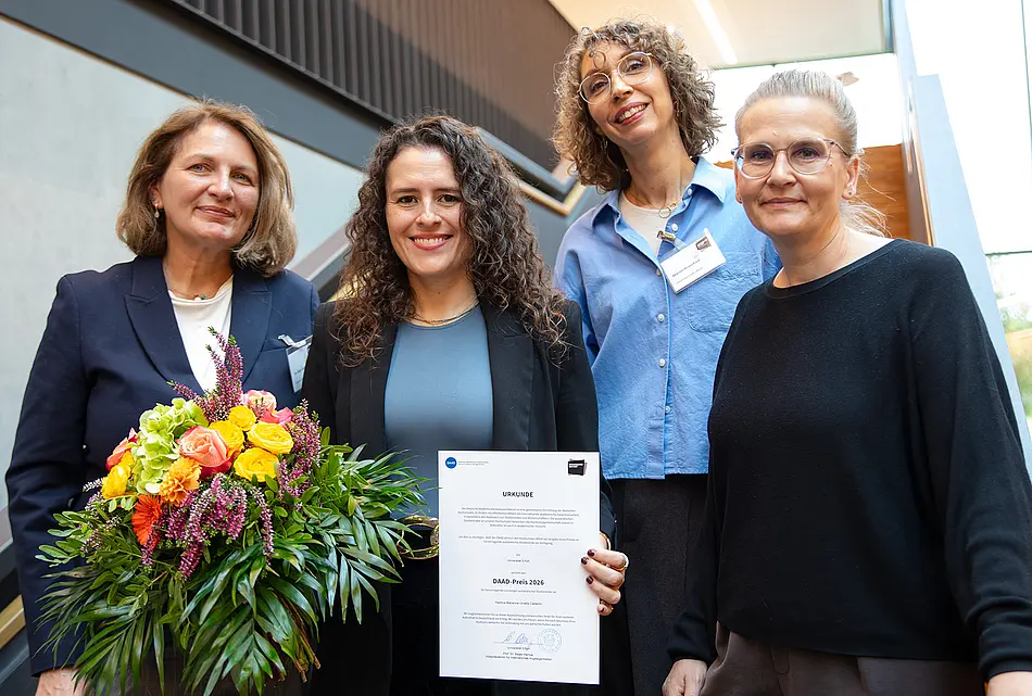 Vier Frauen auf einer Treppe, eine hält Blumen und Zertifikat DAAD-Preis in der Hand: Dr. Antje Dallmann, Leiterin Internationales Büro, Dr. Yeshica Marianne Umaña Calderón, Preisträgerin des DAAD-Preises 2026 der Universität Erfurt, Marion Kraushaar, Stellvertretende Leiterin Internationales Büro und Inga Hettstedt, Hochschulbeauftragte der Stadt Erfurt 