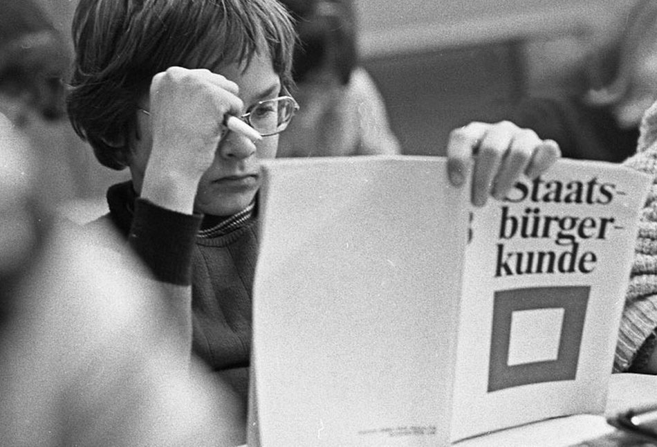 Schüler im Staatsbürgerkundeunterricht der Klasse 8 in den 1970er Jahren, Schüler:in blättert in Schulbuch mit Aufschrift "Staatsbürgerkunde"