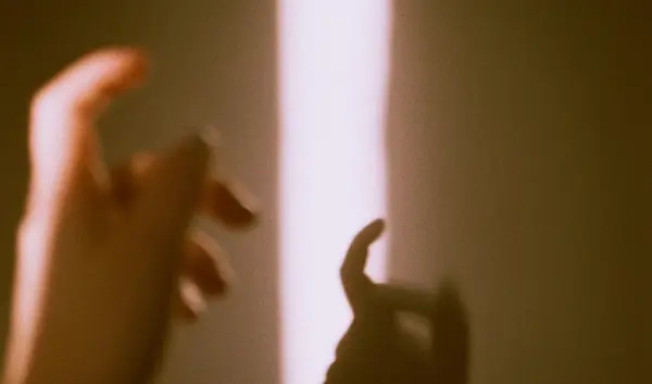 Hände greifen nach einem leuchtenden, sich öffnenden Spalt in einer Wand