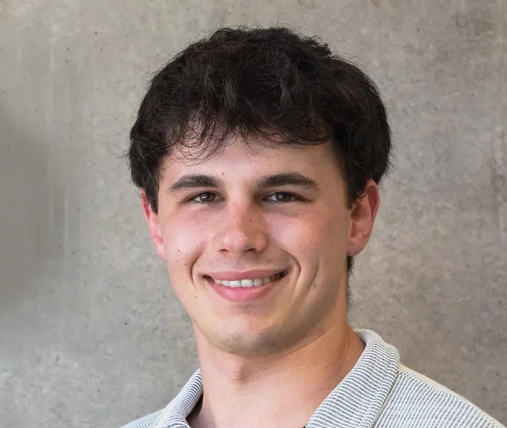 Porträtfoto von Kamil, internationaler Student aus Krakau, lächelnd in kamera, helles Hemd mit Kragen und schwarze, leicht lockige Haare, vor grauem Hintergrund