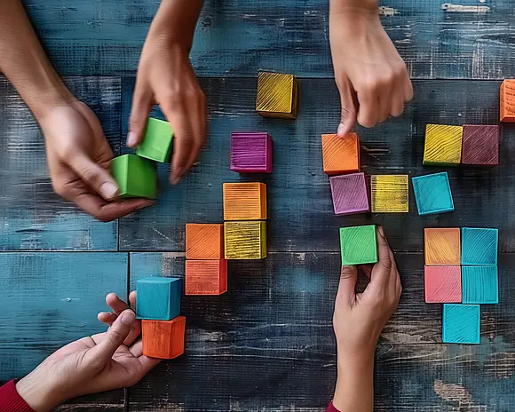 Mehrere Hände legen quadratische bunte Würfel zu einer Gestalt zusammen