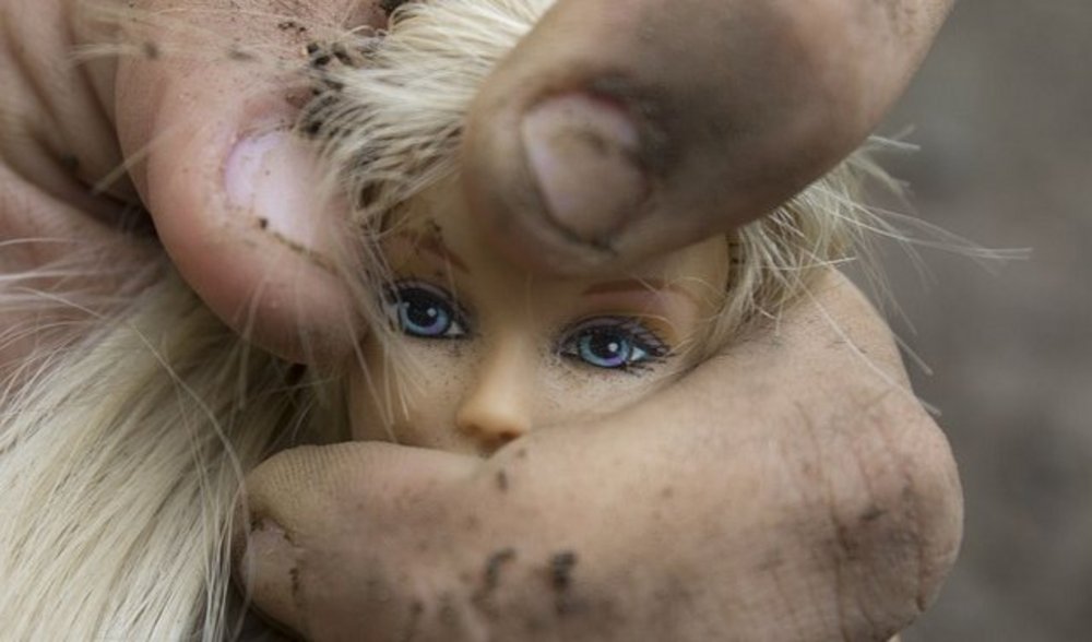 Der Kopf einer Barbiepuppe wird in der Hand eines Manns zerdrückt