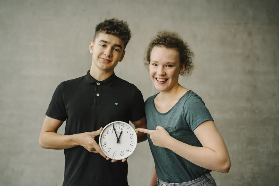 Ein Student und eine Studentin zeigen auf eine Uhr.