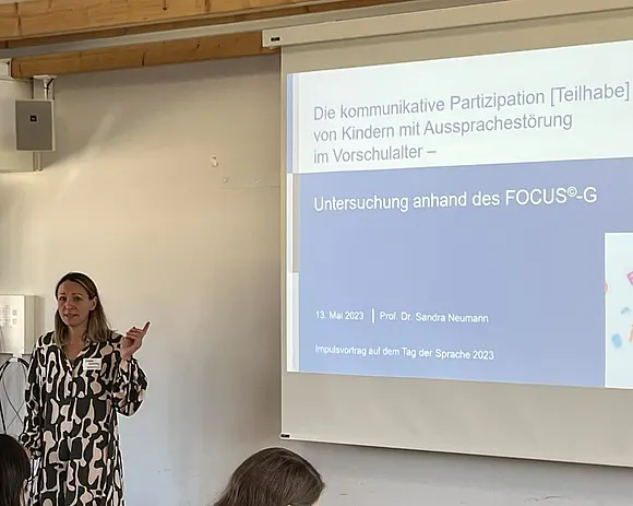 Sandra Neumann steht neben einem Beamerbild und hält einen Vortrag