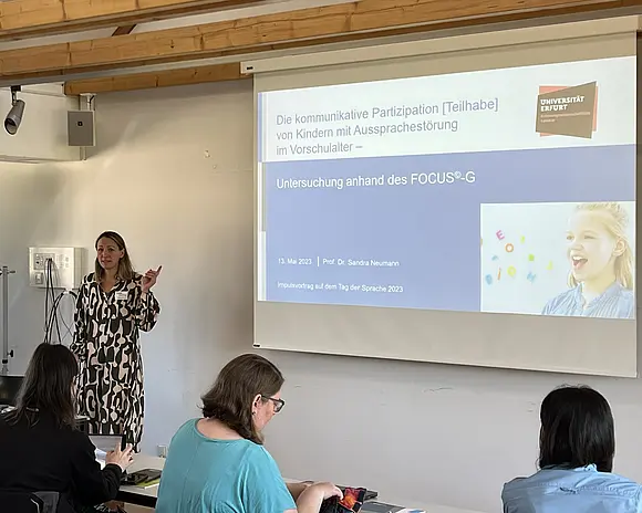 Sandra Neumann hält einen Vortrag. Sie steht neben der Powerpoint Anzeige. 