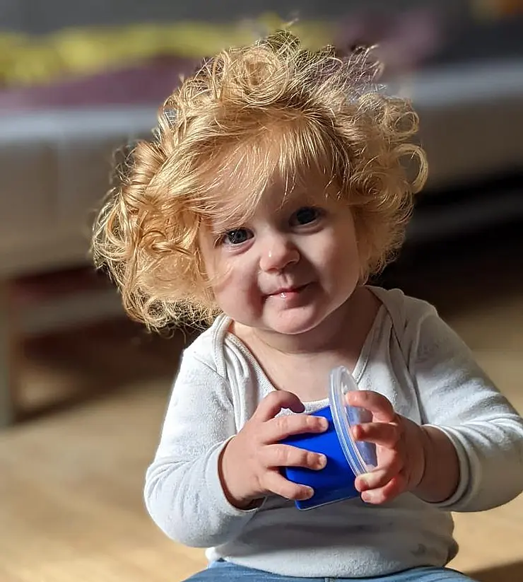 Foto von einem kleinen blonden Kind auf dem boden sitzend mit einer blauen Dose in der Hand