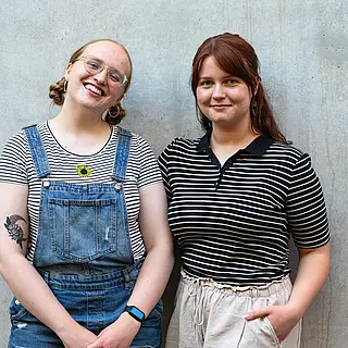 Weronika und Alicia lächelnd vor einer grauen Betonwand