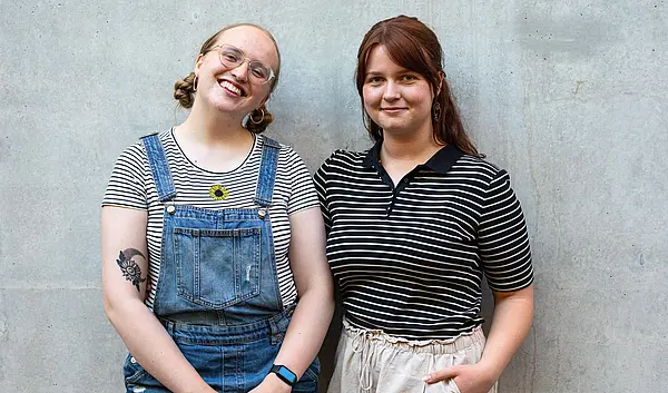 Weronika und Alicia lächelnd vor einer grauen Betonwand