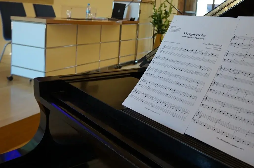 Klavier, auf dem Notenblätter liegen, im Hintergrund das Rednerpult des Coelicums der Uni Erfurt