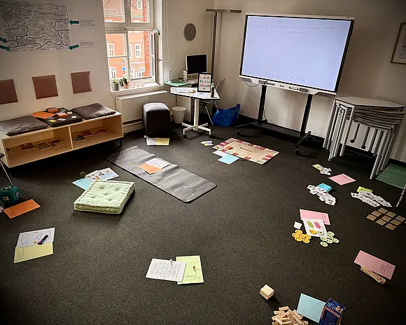 Der kleine Seminarraum. Af seinem grauen Teppichboden sind vielfältige Fördermaterialien zur Ansicht ausgebreitet.