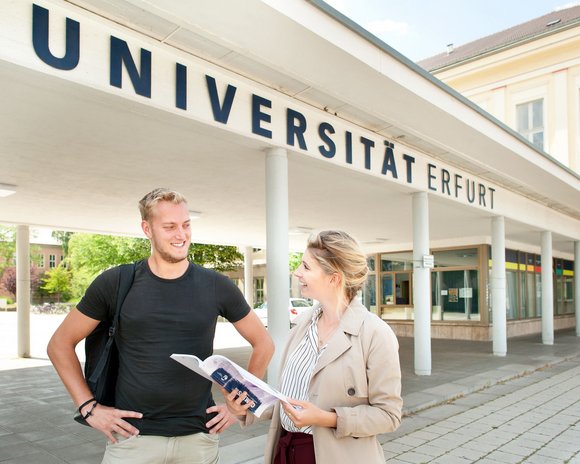 Ein Student und eine Studentin stehen vor dem Haupteingang der Universität Erfurt