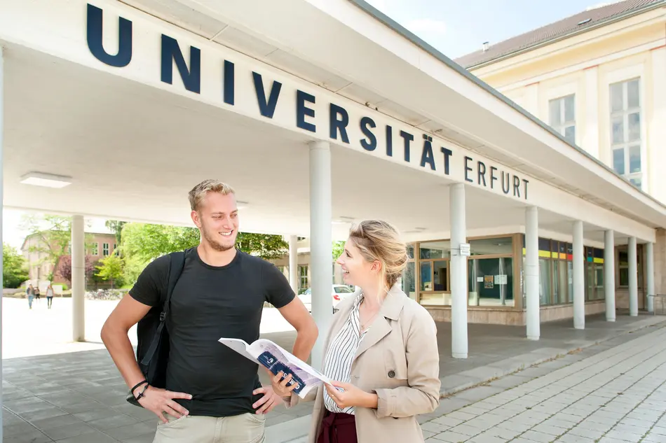  A male and female student stand in front of the main entrance to the University of Erfurt.