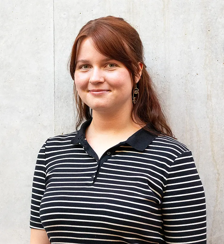 Alicia, leicht seitlich, mit braunen offenen Haaren und einem schwarzen Streifen-Oberteil