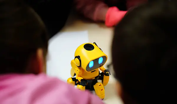 Ein kleiner gelber Roboter steht auf einem Tisch und ist umringt von Kindern