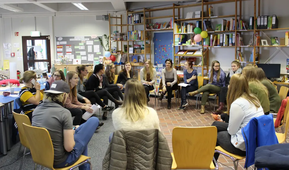 Studierende der Universität Erfurt und Siegen sitzen in einem Stuhlkreis in der OASE Lernwerkstatt in Siegen im Rahmen eines gemeinsamen Seminars