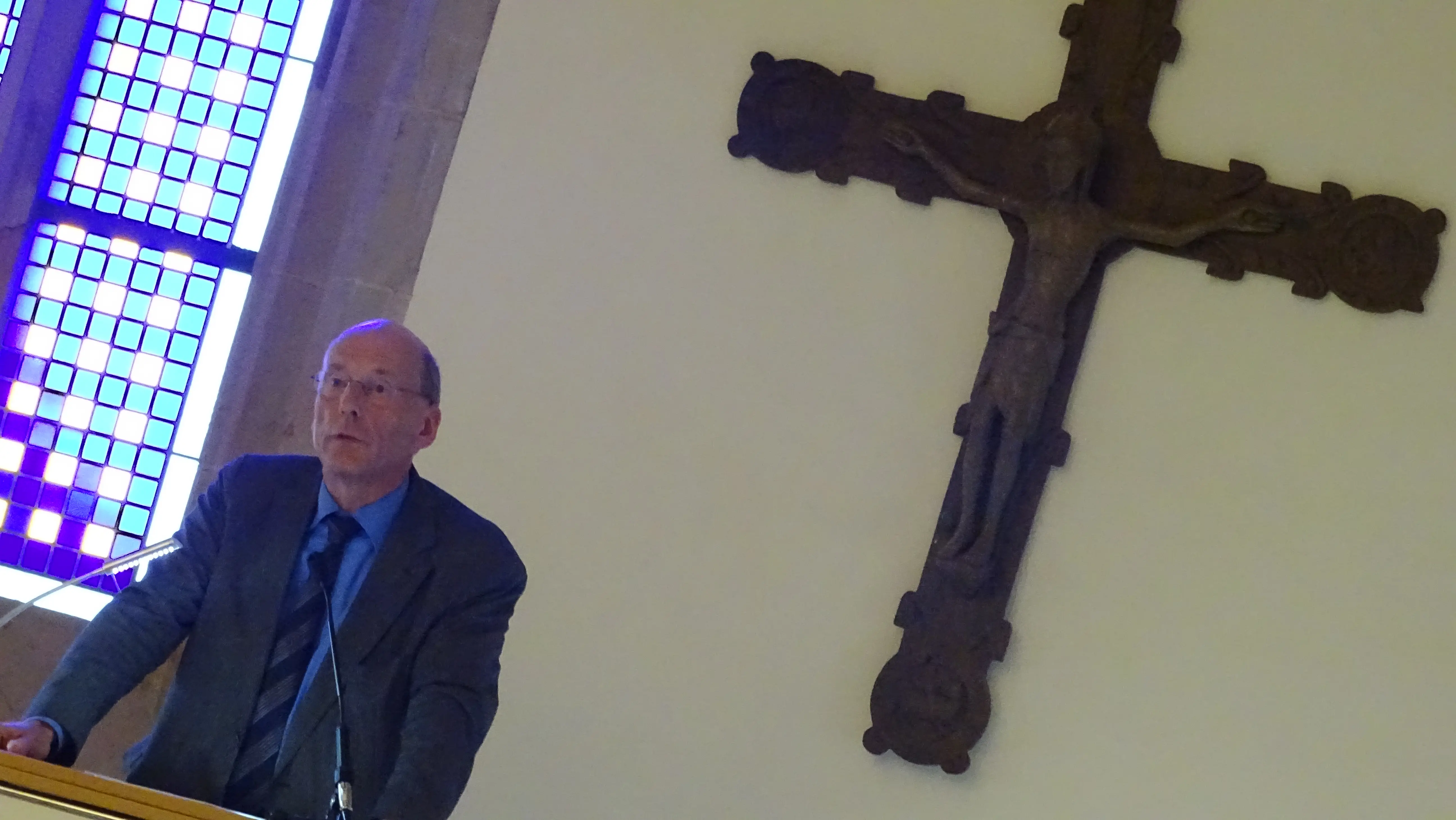 Prof. Dr. Eberhard Tiefensee während seiner Abschiedsvorlesung, im Hintergrund das Holzkreuz im Coelicum