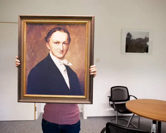 A person holding a painting of Franz Haniel in front of them