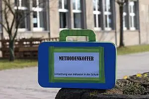 gebastelter Koffer mit der Aufschrift "Methodenkoffer" vor dem Gebäude der Lernwerkstatt