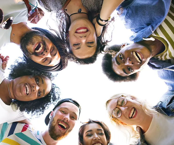 Junge Erwachsene schauen im Kreis von oben runter in die Kamera