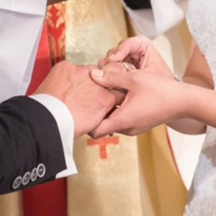 Eine Frau steckt ihrem Mann vor dem Altar den Ehering an